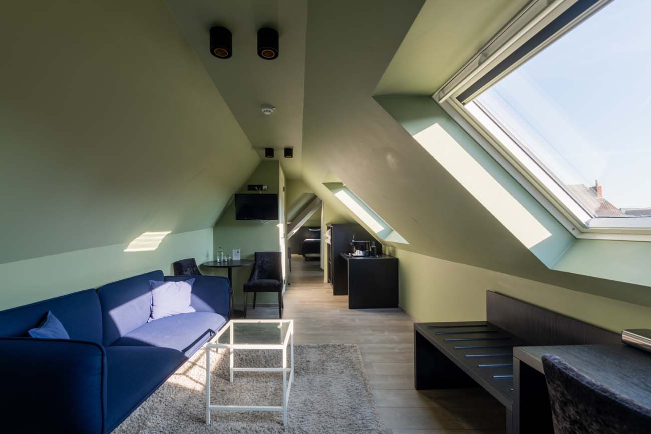 Zithoek met blauwe sofa en werkplek onder de dakramen